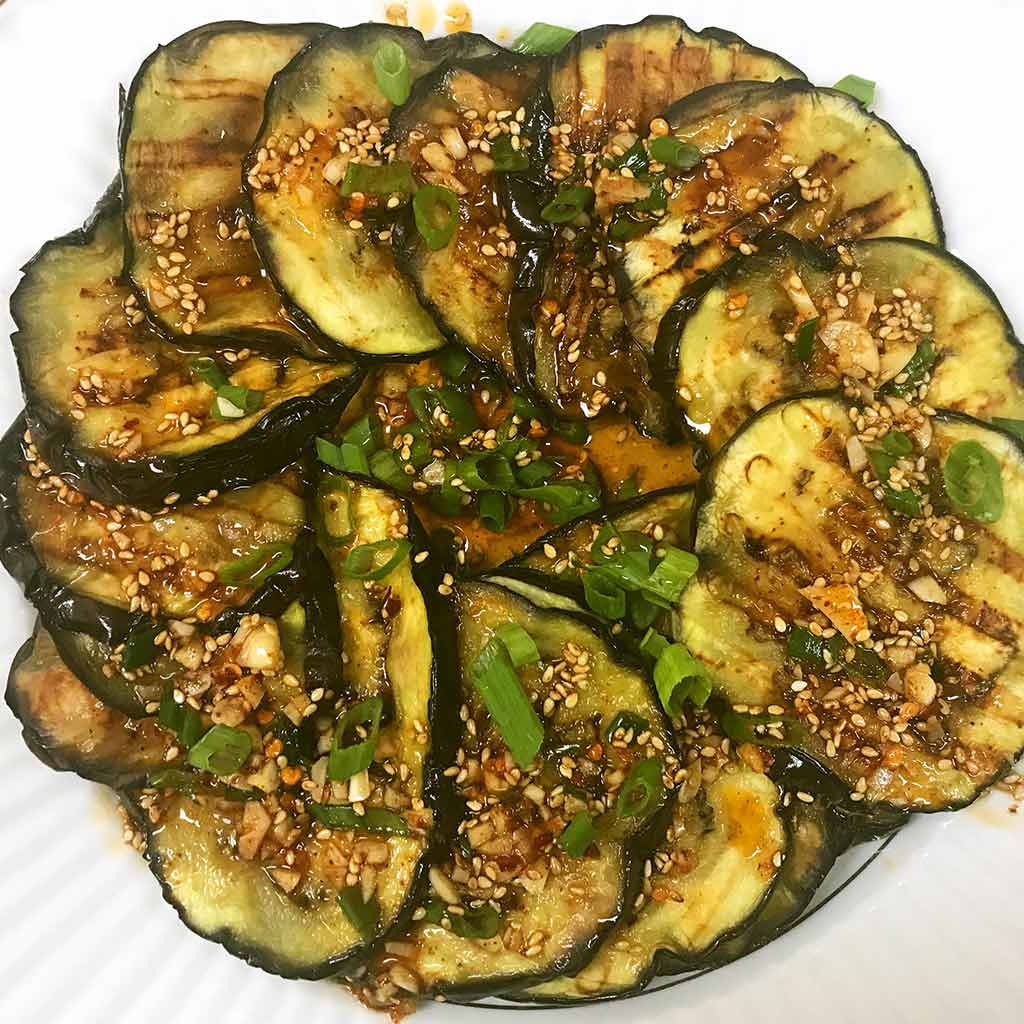 grilled egg plant, with brown grill mark. On top there is spicy garlic sesame sauce and green onion