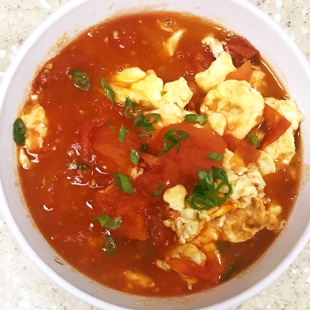 Stir-fried tomato and scramble egg. Scrambled eggs are soaking in the tomato sauce, garnish with green onion.